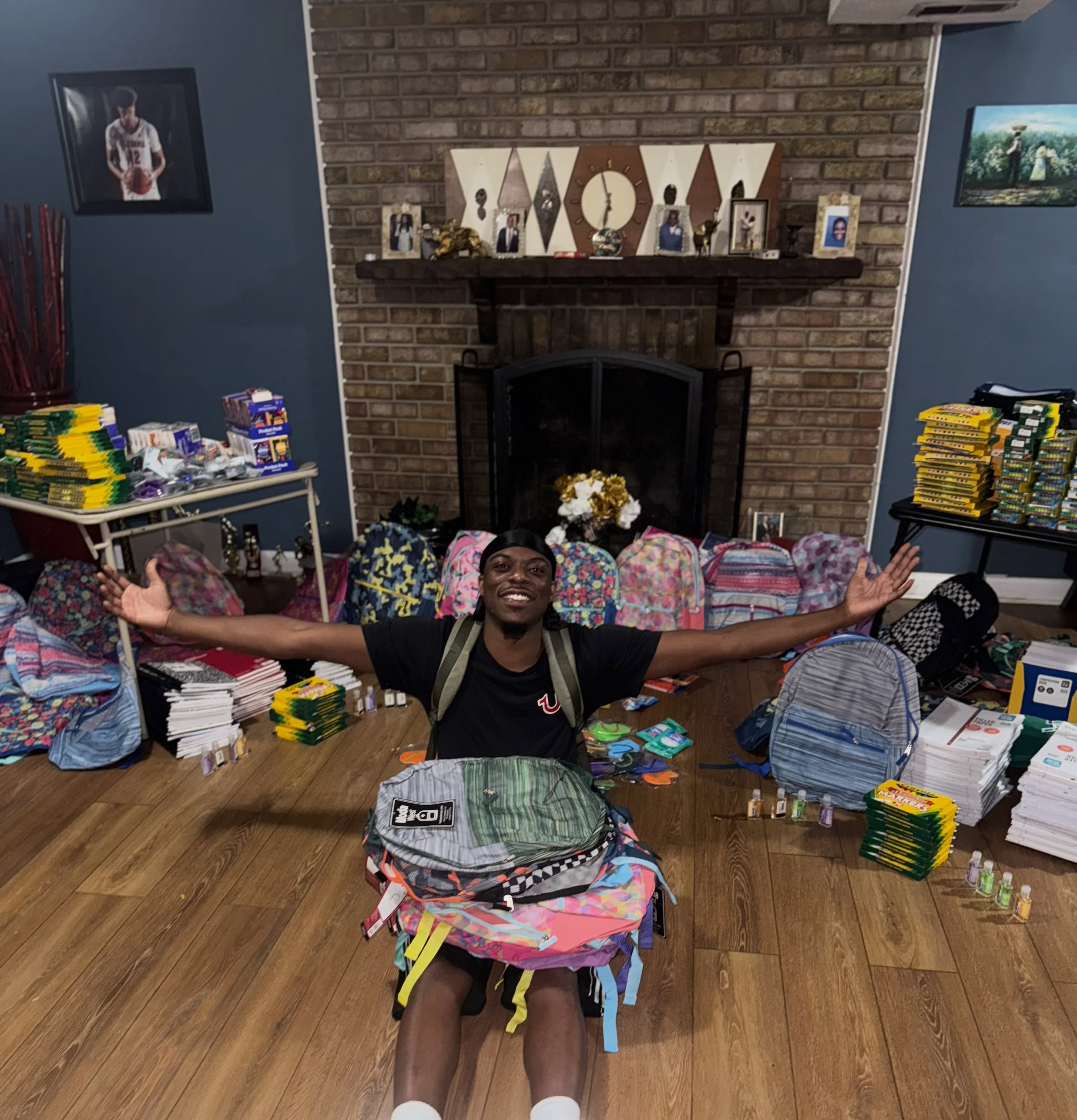 Big Boost sitting on the floor surrounded by backpacks and school supplies for his Capitol Heights giveaway
