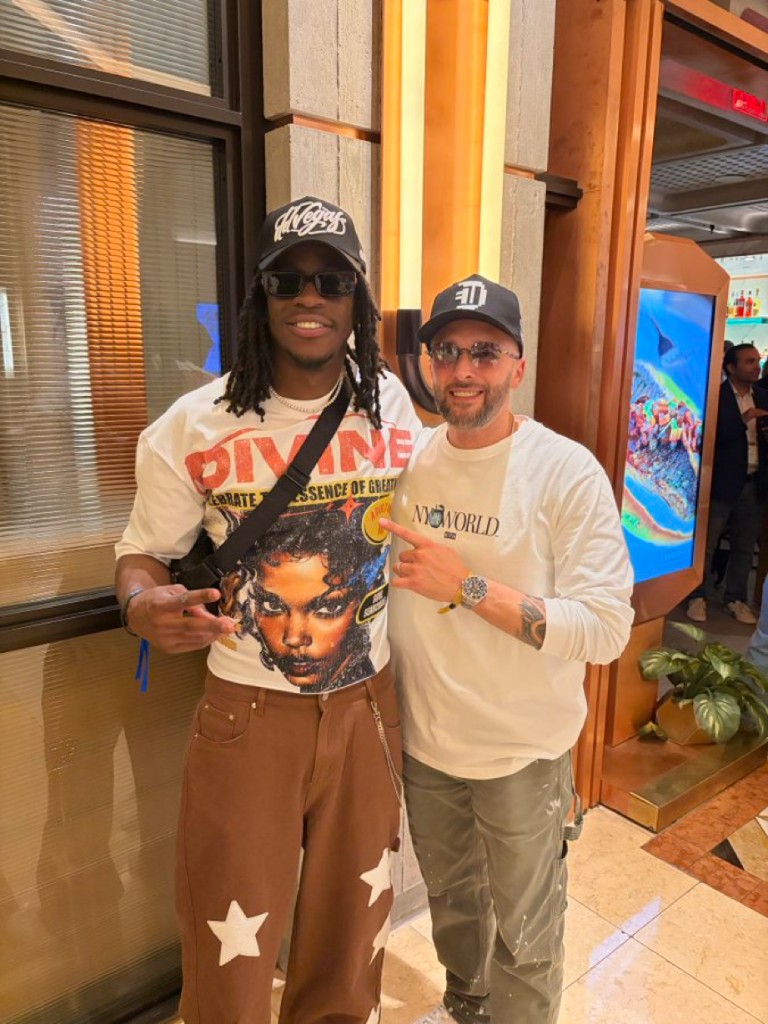 Motion wearing a Divine graphic t-shirt and star-patterned pants, posing with a friend at an event